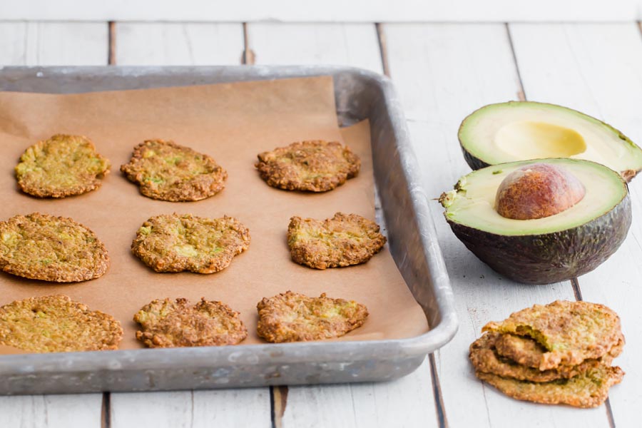 avocado chips on a sheet pan next to a avocado