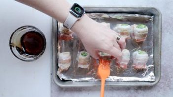 brushing maple syrup with an orange silcone brush on top of a bacon wrapped sprout