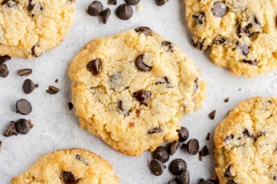 five golden brown chocolate chip cookies on the table with dark chips spread around