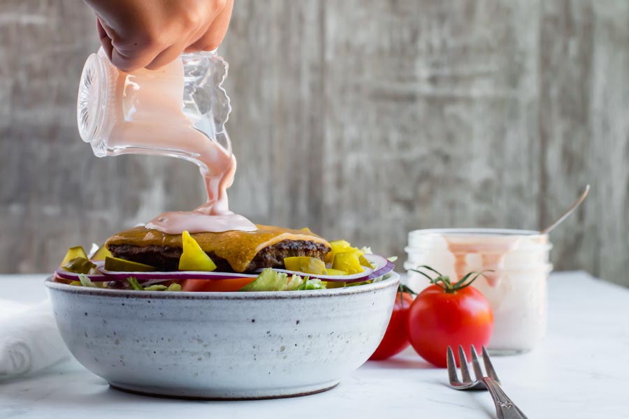 pouring keto thousand island dressing on burger bowl