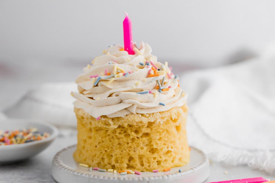 a large vanilla cupcake with buttercream frosting and mulit colored sprinkles