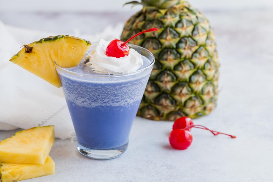 a single blue hawaiian cocktail topped with whipped cream, a cherry and a pineapple slice