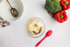 Salad dressing ingredients in a small bowl next to a red spoon.