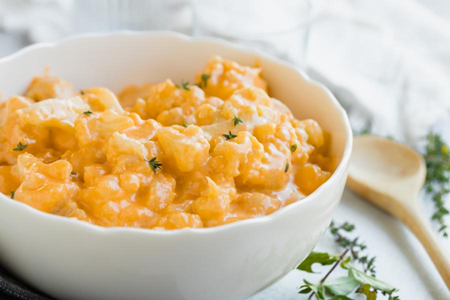 a white bowl with creamy cheese covered cauliflower topped with herbs