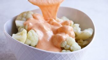 pouring a cheese sauce over cooked cauliflower