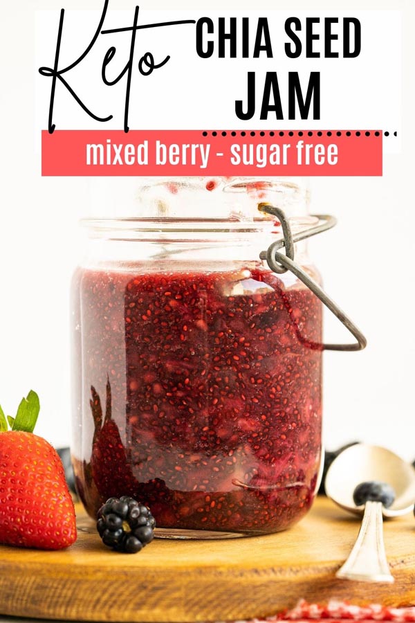 a big jar of mixed berry jam next to a spoon and a couple of berries