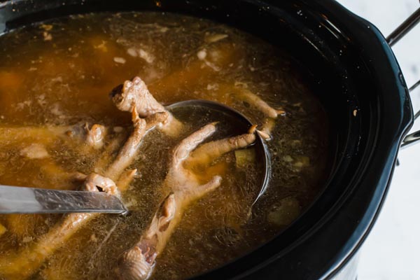 cooked bone broth in a slow cooker with chicken feet