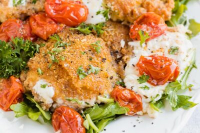 Crispy chicken topped with pepper and parsley next to melted burrata cheese and tomatoes.