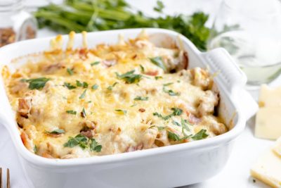 cheesy casserole in a white casserole dish topped with parsley with a glass of white wine next to it