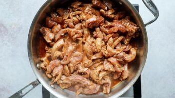 Sliced chicken thighs cooking in a skillet.