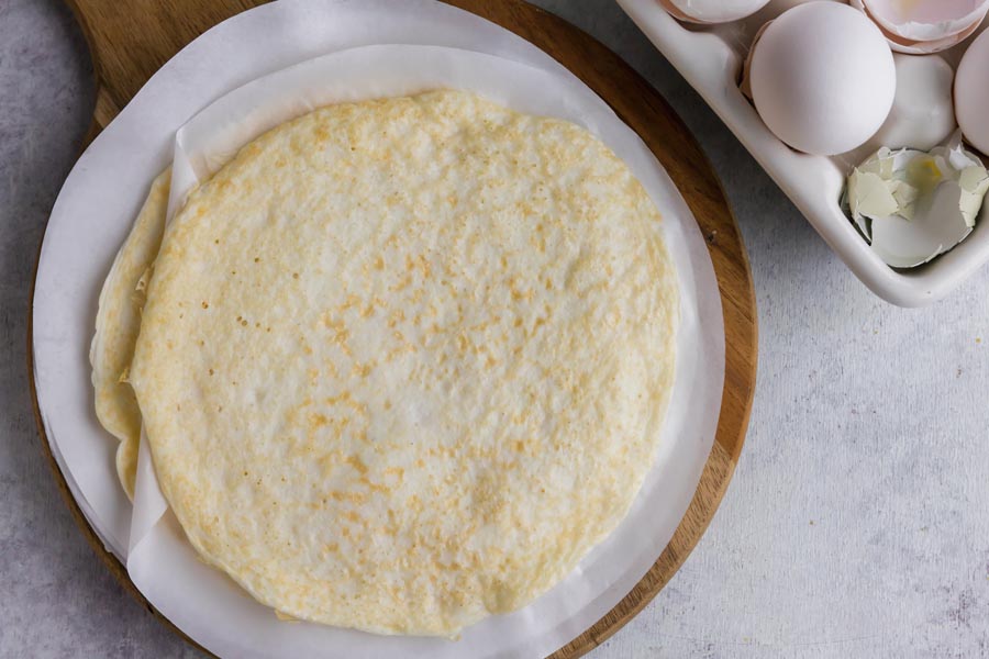 Looking down on a stack of egg wraps on a cutting board next to a carton of eggs.