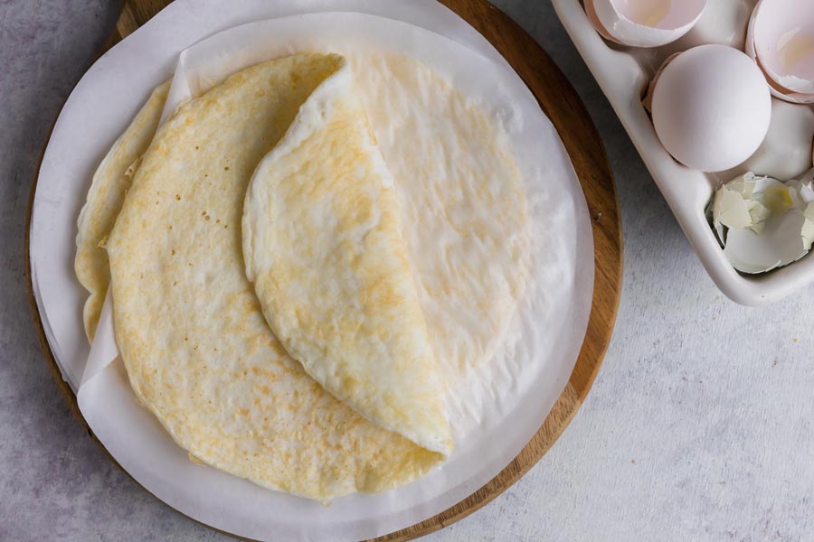 A wrap made of egg folded on itself on parchment paper next to cracked egg shells.