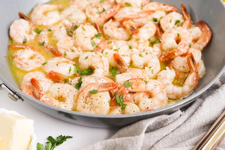 perfectly cooked shrimp sitting in a skillet with melted butter and parsley