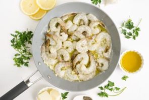 raw shrimp and butter in a skillet with fresh parsley around