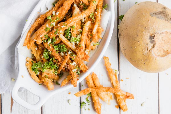 a basket of keto jicama fries with garlic, parmesan and parsley sprinkled on top