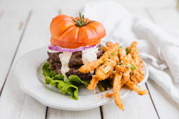 bunless burger with a tomato on top next to a mound of garlic parmesan jicama fries