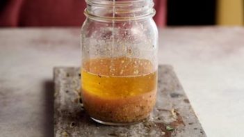 pouring olive oil into a dressing sitting in a mason jar