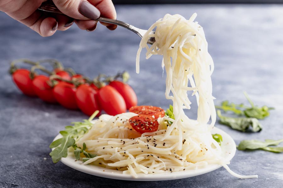 holding a forkful of noodles over a plate of more noodles