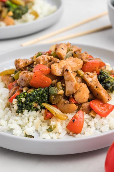 A dinner plate with stir fried chicken, broccoli and peppers over cauliflower rice.