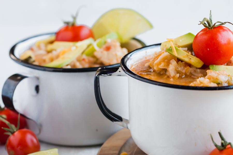 two white mugs with black lining filled to the brim with keto chicken and rice topped with a stemmed cherry tomato