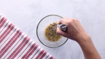 A hand whisking a butter mixture with black sesame seeds.