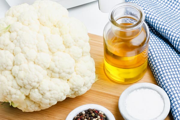 a whole cauliflower head on a cutting board with olive oil and peppercorns