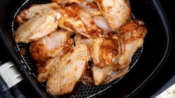 Party wings coated with seasoning sitting in an air fryer basket.