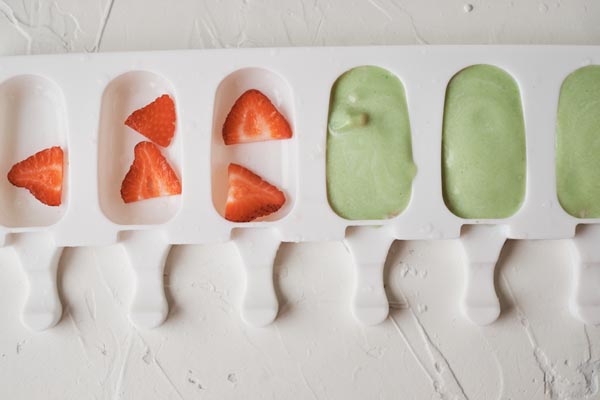 sliced strawberries fill one side of the popsicle mold and avocado mixture is in the other side