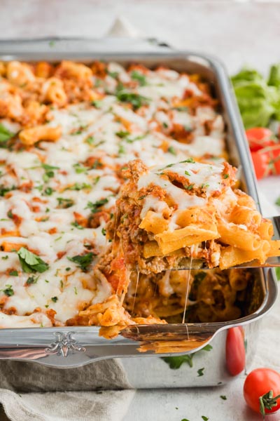 A spatula pulling out a serving of ziti pasta with beef and marinara while cheese pulls from the dish.