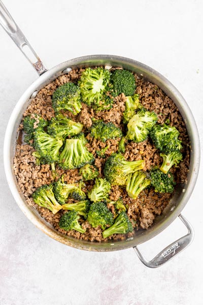 an all clad skillet with ground beef and broccoli florets spread throughout