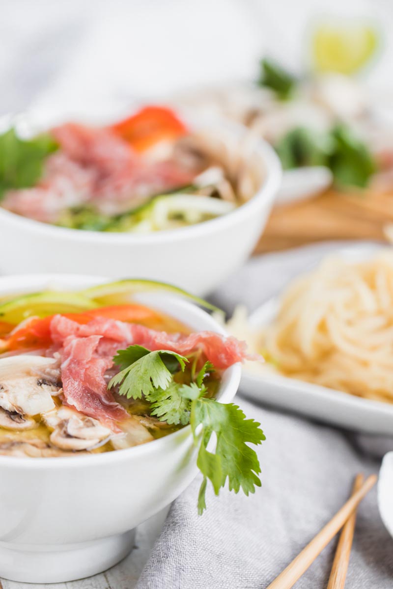 cilantro and shaved beef lying on bone broth with chop sticks nearby