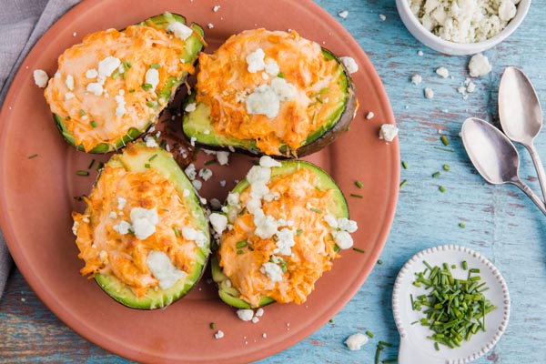 overhead shot of four stuffed avocados on a red plate with chives sprinkled all around