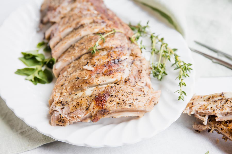 side angle view of cooker pork ribs on a white plater with herbs near