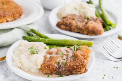 crispy chicken fried steak on a plate with gravy on top and a couple of keto sides