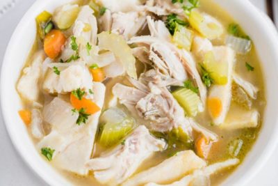 overhead view showing shredded chicken, veggies and noodles in a broth