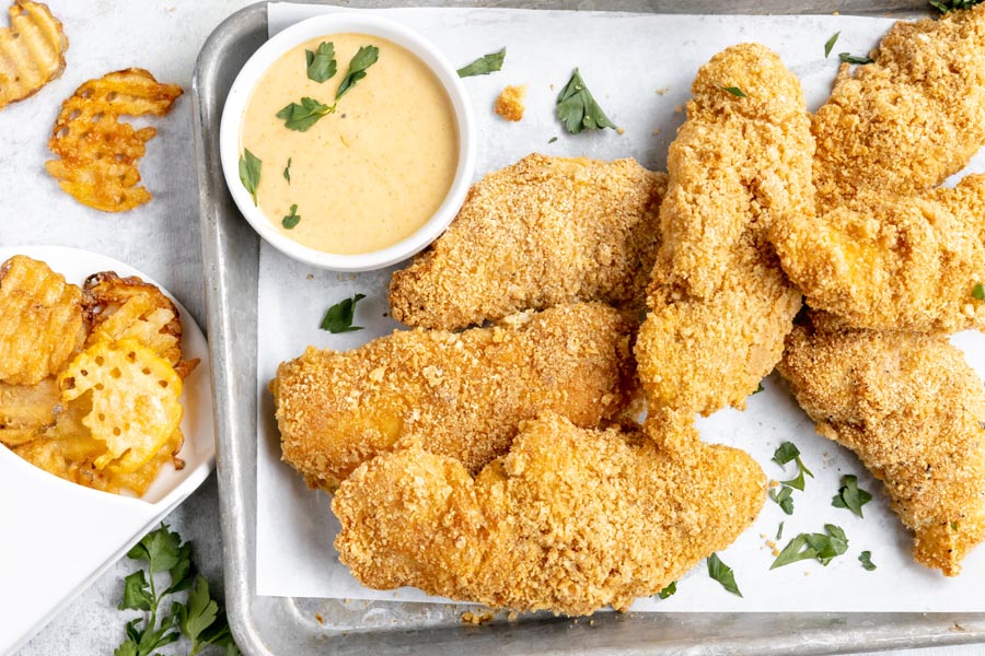 a tray with a bunch of baked chicken strips next to waffle fries and chick-fil-a sauce