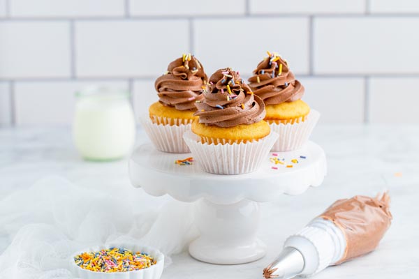 three cupcakes with chocolate buttercream frosting decorated with sugar free sprinkles and a piping bag near