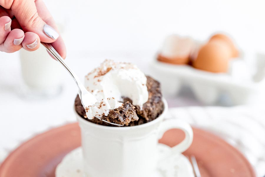 a hand holding a fork containing a piece of keto cake with whipped cream on it