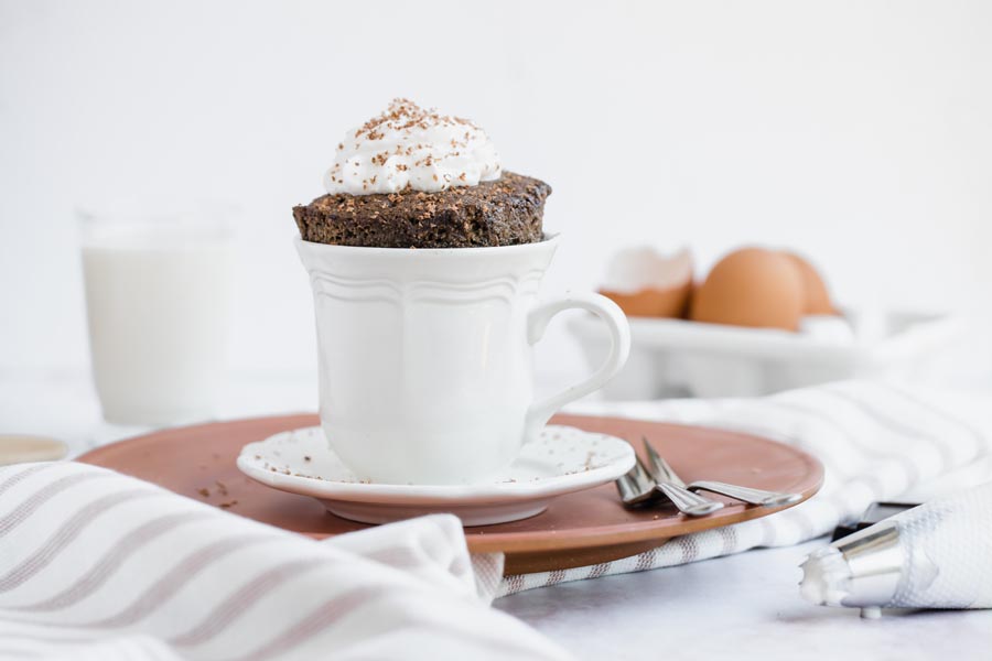 chocolate cake sticking out of a small mug with striped napkins nearby and a piping bag with whipped cream