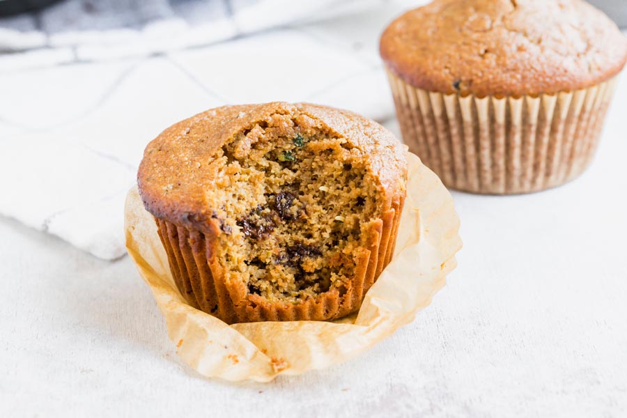 two muffins the closest one has a bite taken out of it with zucchini and chocolate chips coming out