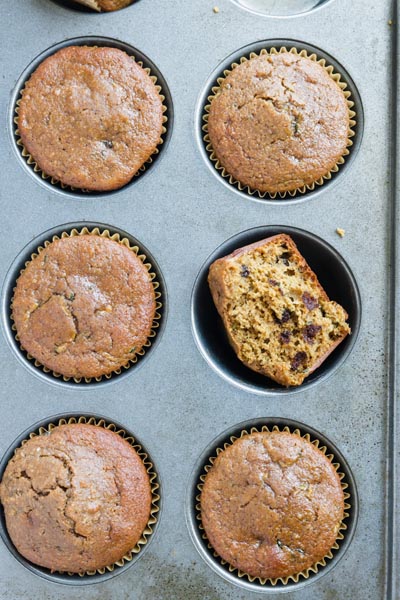 six chocolate muffins in a muffin tin with one cut in half on facing up