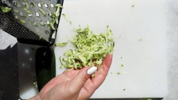 holding grated zucchini next to a cheese grater