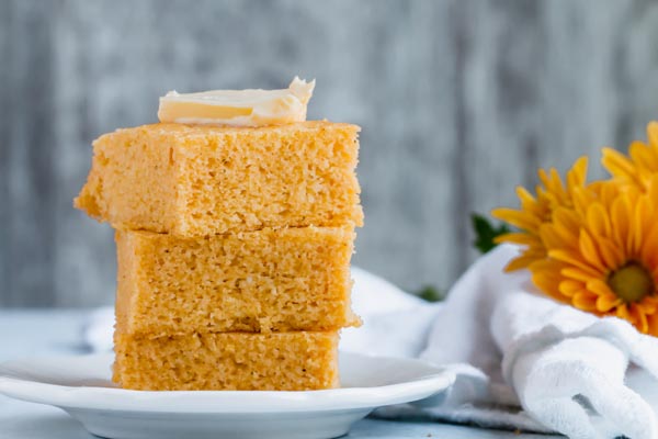 stack of keto cornbread with butter sitting next to flowers