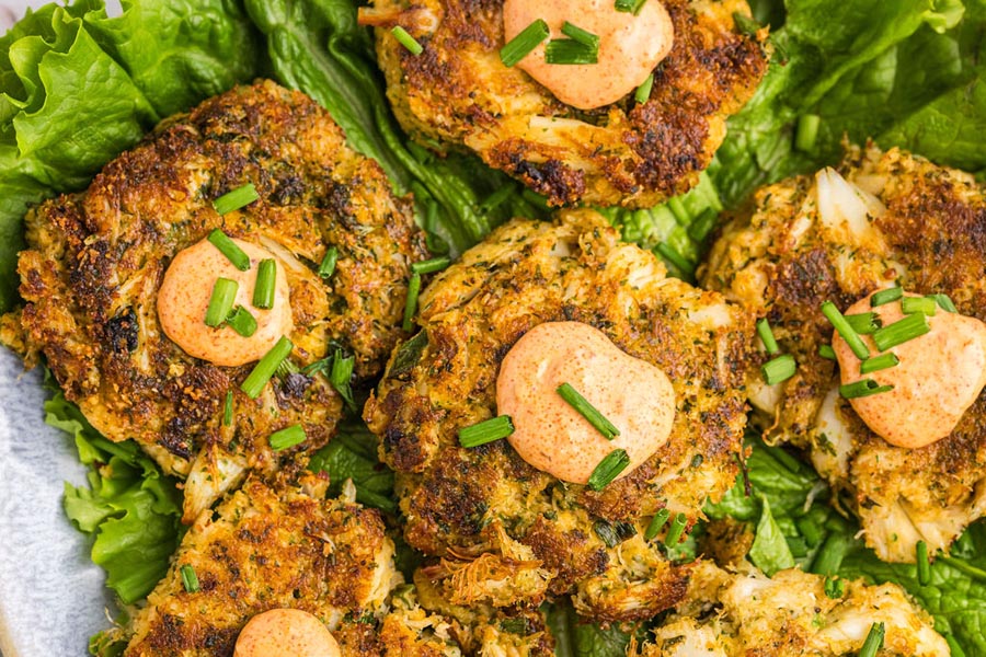 Fried crab cakes on a bed of lettuce and topped with remulade sauce and chives.