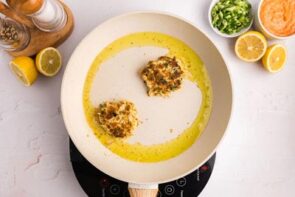 Two crab cakes frying in a skillet.