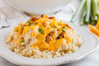 a plate of cheesy crack chicken topped with green onion and bacon over a bed of cauliflower rice