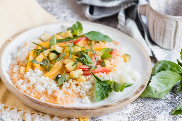 a plate of red curry sauce over cauliflower rice and vegetables next to some tea