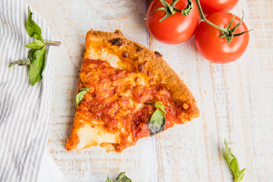 a slice of thick crust keto pizza next to tomatoes and basil