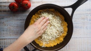 layering shredded mozzarella cheese on top pizza dough