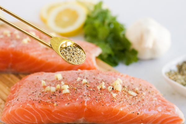 sprinkling black pepper on a salmon fillet